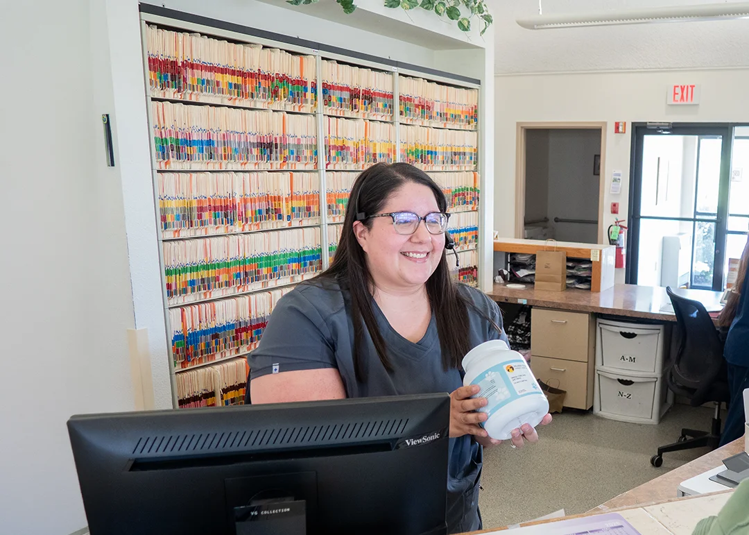A customer service representative holds a container of supplement by the front desk of the office