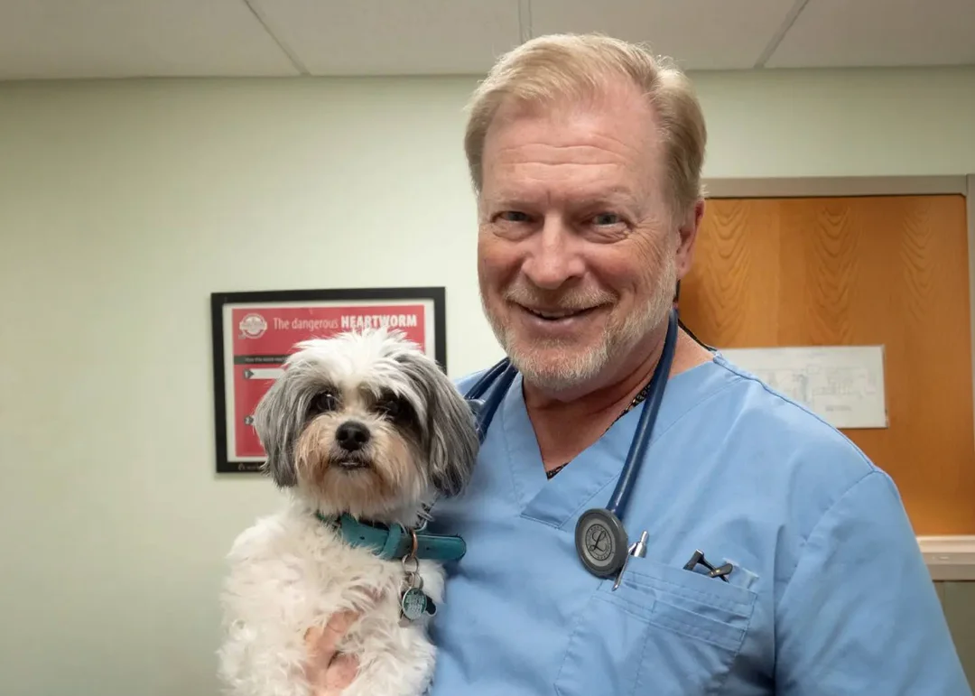 A veterinarian smiles for a picture with a small white dog